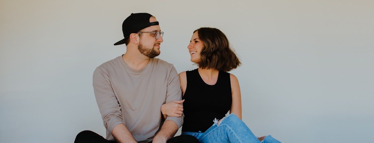 Jon and Katherine sitting together against a white wall