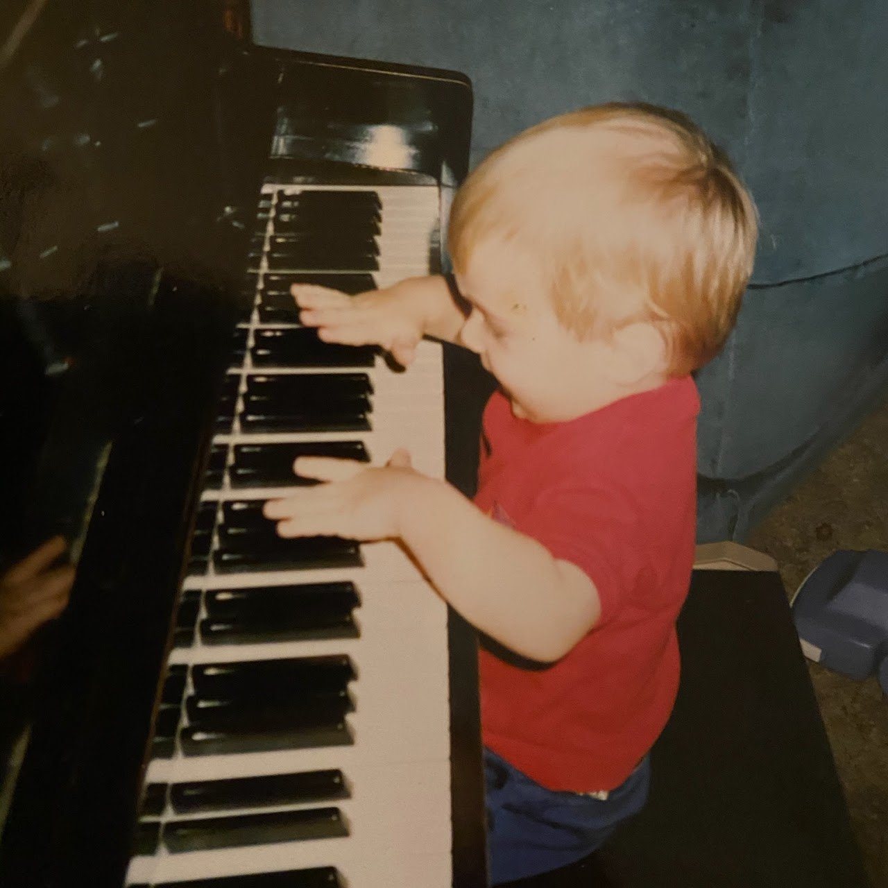 A toddler in a red shirt playing an upright piano