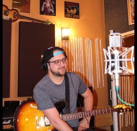 Jon sitting with an electric guitar in a home studio with a microphone
