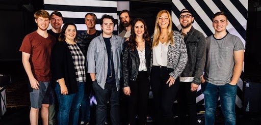 Jon standing with a group of about ten worship team members in front of a striped stage backdrop